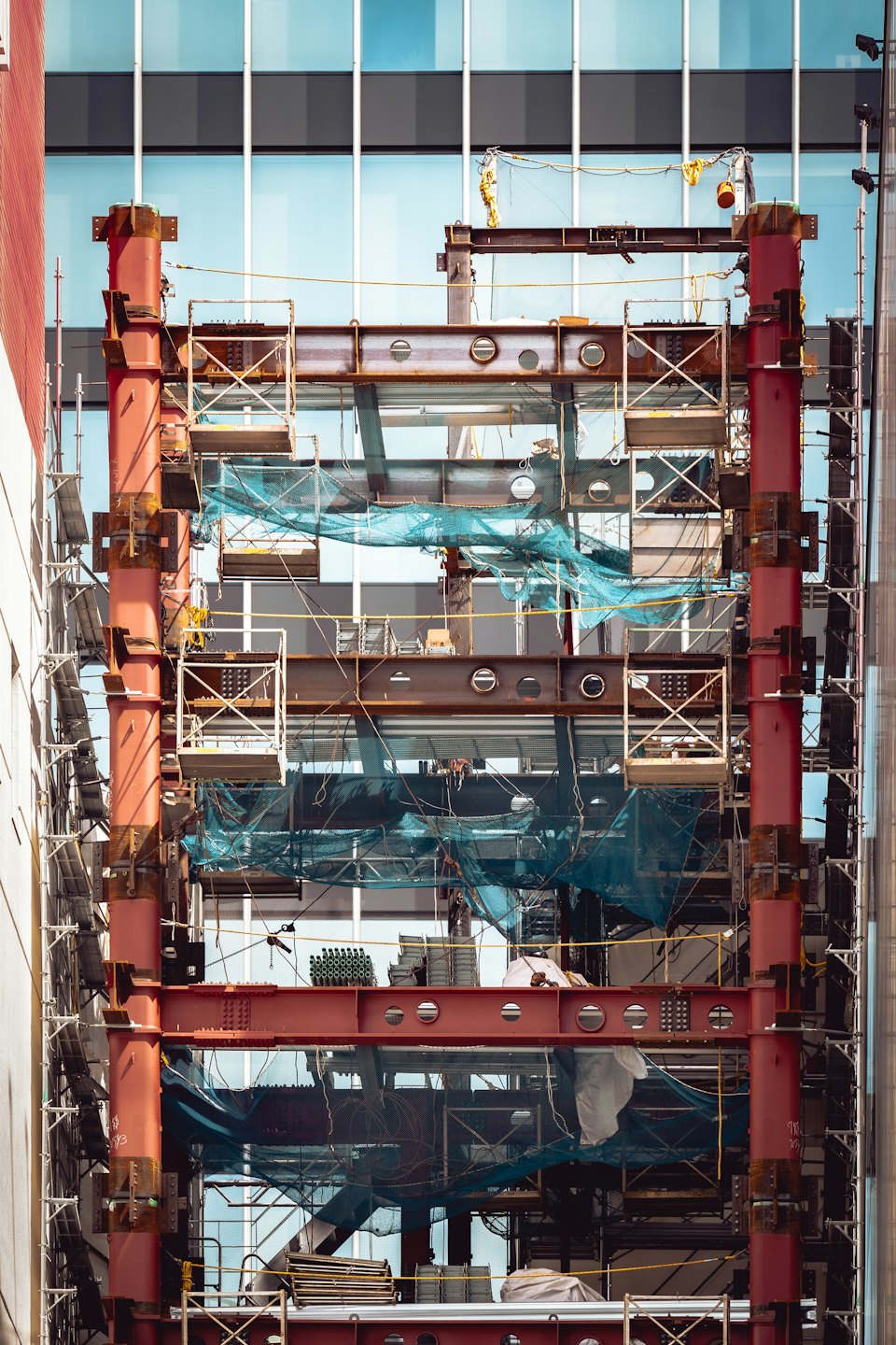 Construction workers build a skyscraper with red steel beams and scaffolding.