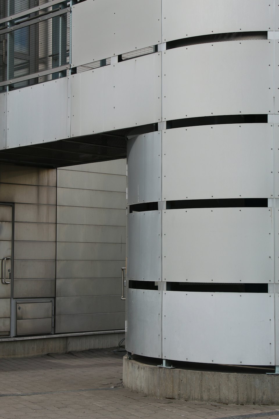 Modern grey metal building facade with curved section and walkway.