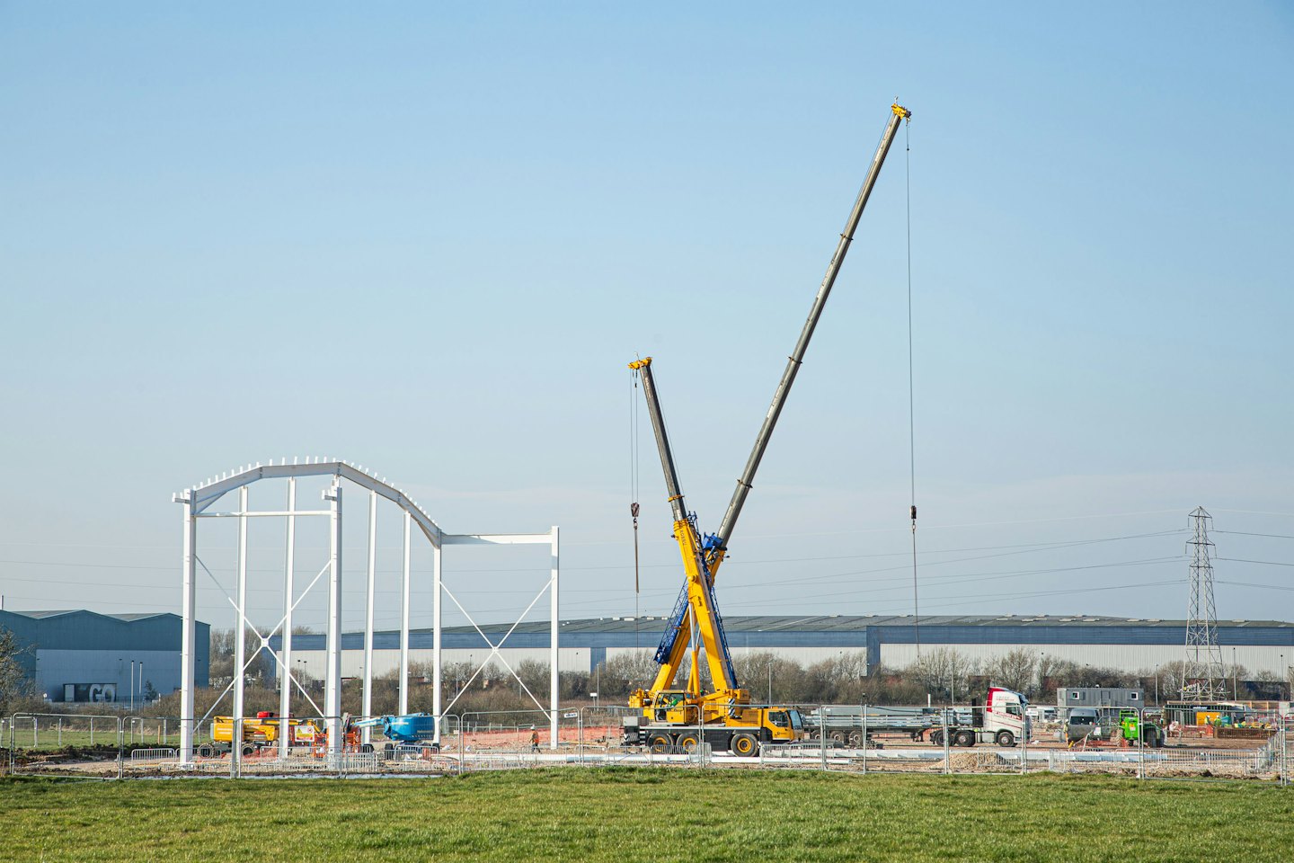 Two yellow cranes stand by a large white metal building frame.